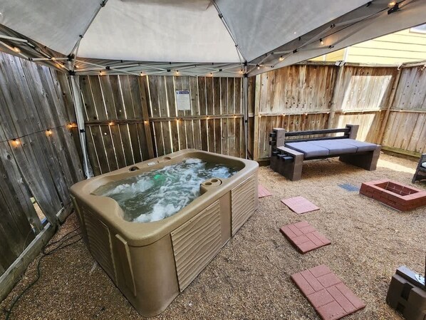 A hot tub under a canopy, surrounded by wooden walls and a bench.