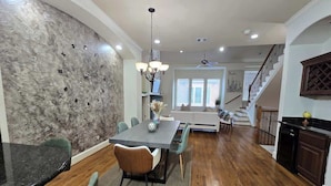 A spacious dining area with a large table, chairs, and a chandelier. There is a staircase leading to an upper level.