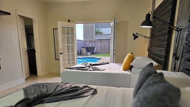 A bedroom with a bed, a bedside lamp, and a view of a backyard with a pool.