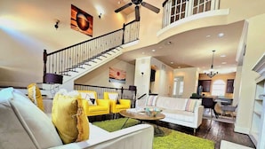A spacious living area with a staircase, a white sofa, yellow chairs, and a green rug.