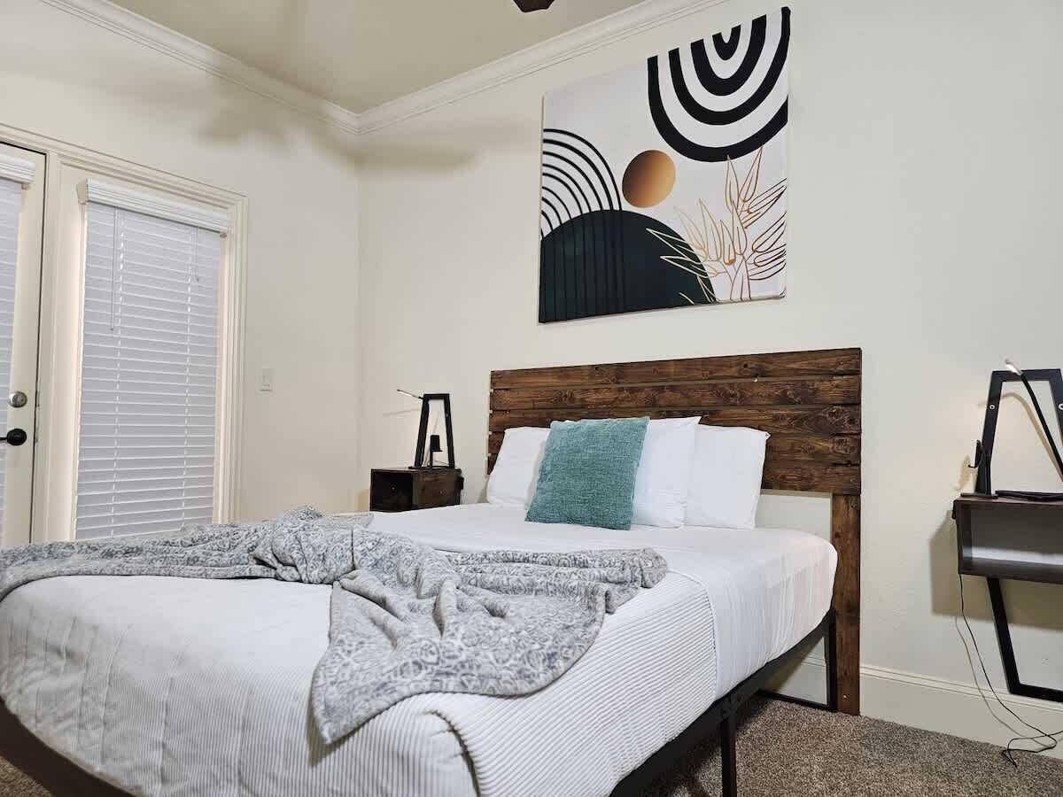 Una camera da letto con un letto, una testiera in legno, un quadro, un comodino e una scrivania.