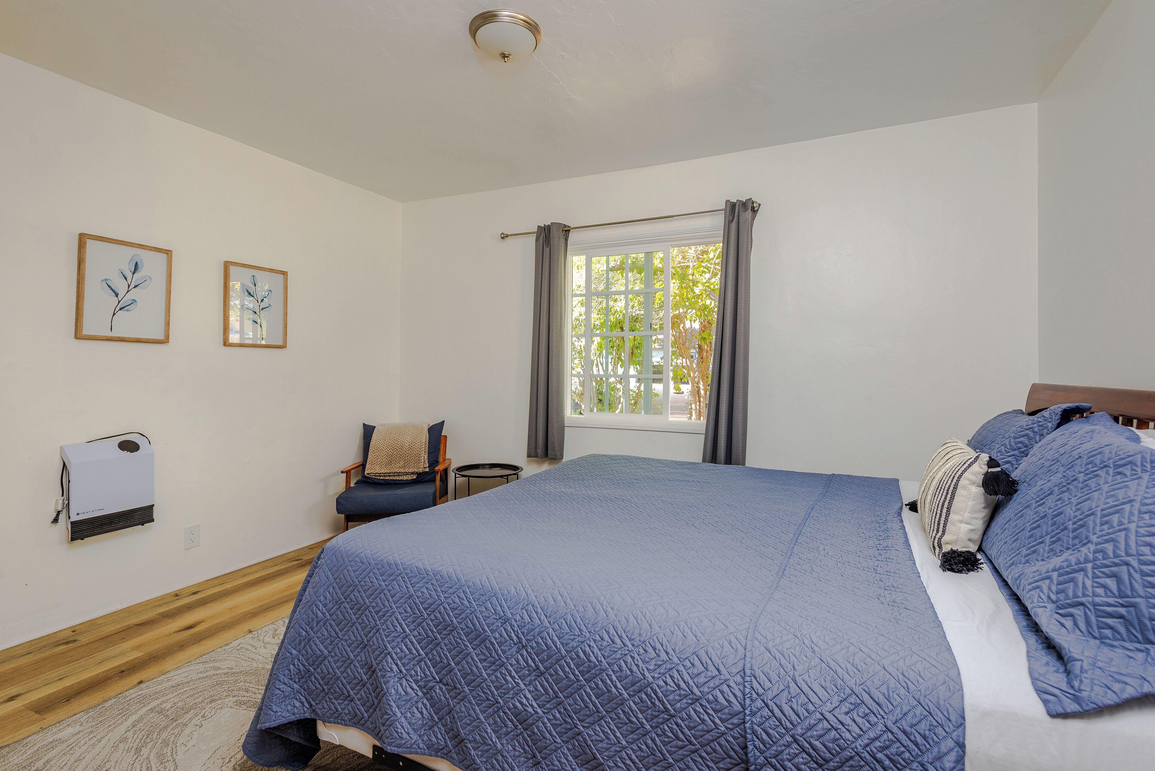 Une chambre avec un grand lit, une fenêtre avec des rideaux, une chaise et deux tableaux encadrés accrochés au mur.