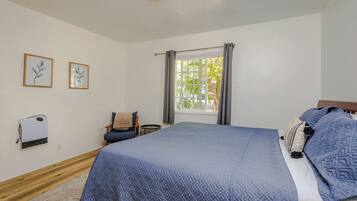 Une chambre avec un grand lit, une fenêtre avec des rideaux, une chaise et deux tableaux encadrés accrochés au mur.