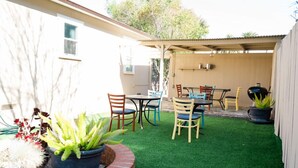 Un patio trasero con césped artificial, una jardinera de ladrillo y una mesa con sillas.