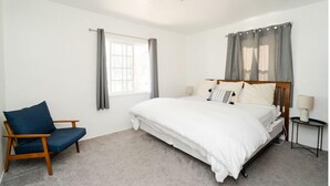 Un dormitorio con una cama individual, una silla, una mesita de noche y una ventana con cortinas.