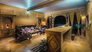 A cozy lounge area with a sofa, a wooden table, and a fireplace. - Sonal Desert Camp Jaisalmer (Jaisalmer)