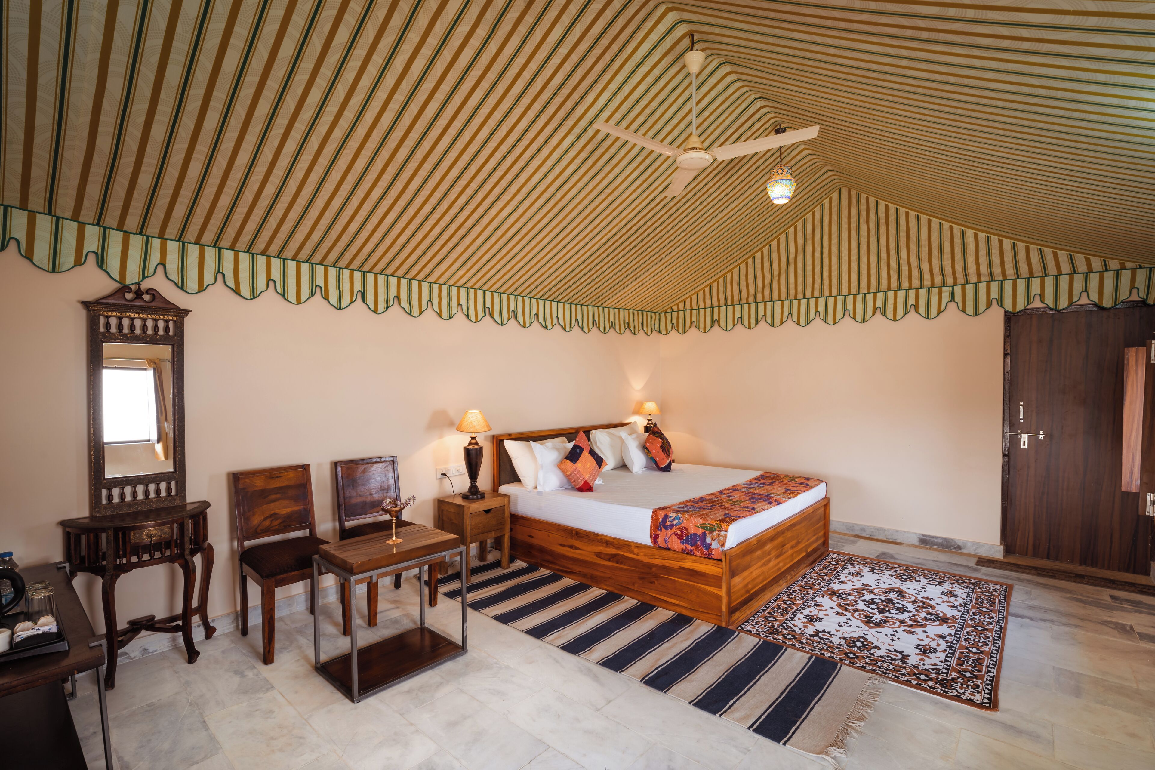A bedroom with a striped ceiling, a bed with pillows, a nightstand, a desk, a chair, a mirror, and a wardrobe.