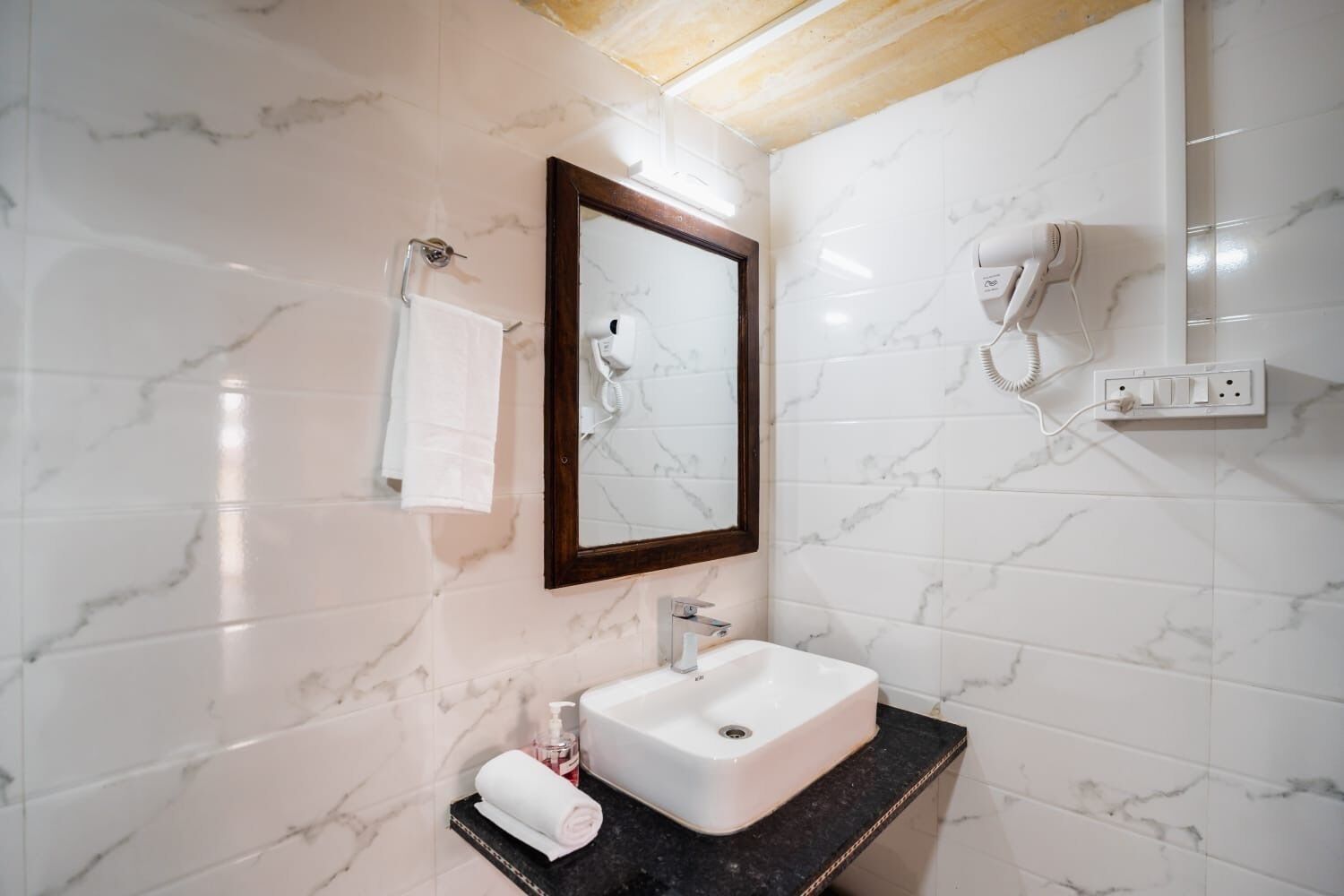 A bathroom with a marble wall, a sink, a mirror, a towel rack, and a hairdryer.