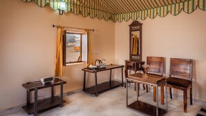 A room with a striped ceiling, a window with curtains, a wooden table with chairs, a clock, and a small table with a projector. - Sonal Desert Camp Jaisalmer (Jaisalmer)