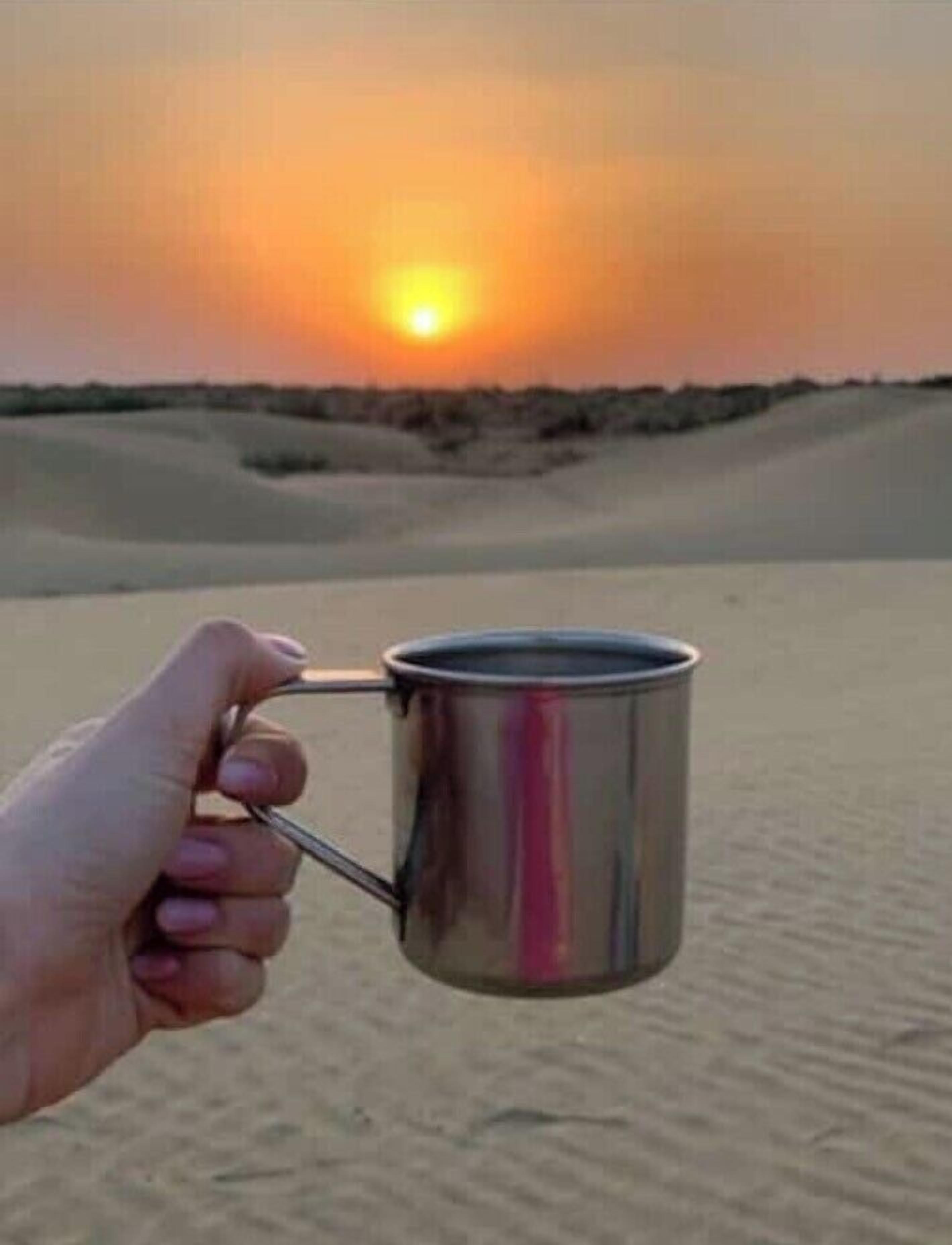 Eine Hand hält eine Edelstahl-Tasse vor einer Wüstenlandschaft bei Sonnenuntergang.