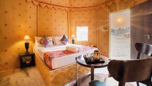 A cozy bedroom with a bed, pillows, a bedside table with a lamp, a chair, and a view of the beach. - Sonal Desert Camp Jaisalmer (Jaisalmer)