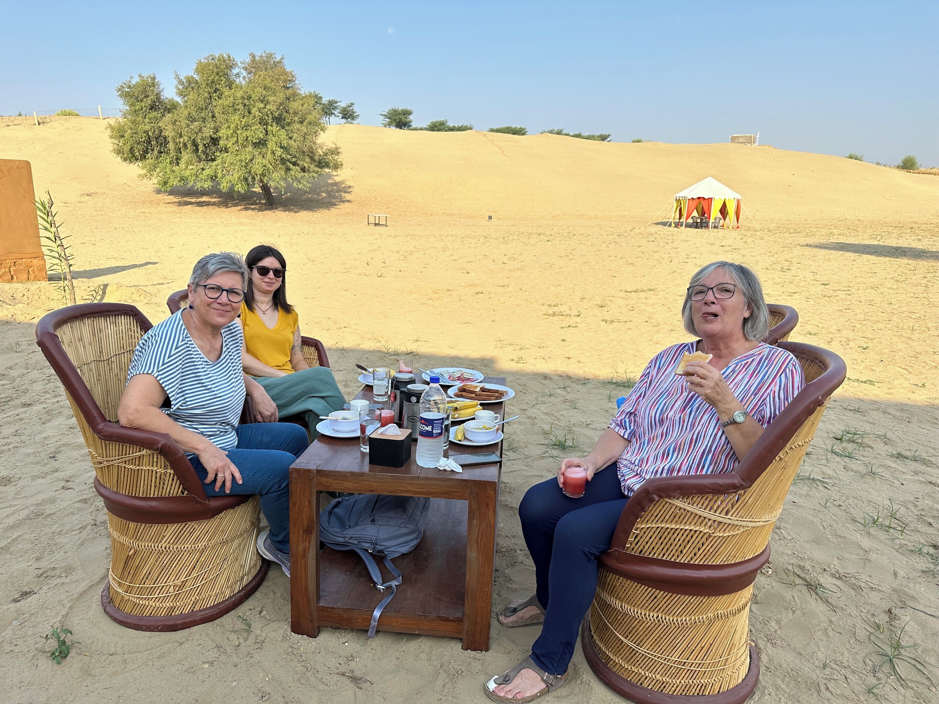 Trois personnes sont assises à une table, devant de la nourriture et des boissons, dans un décor désertique.