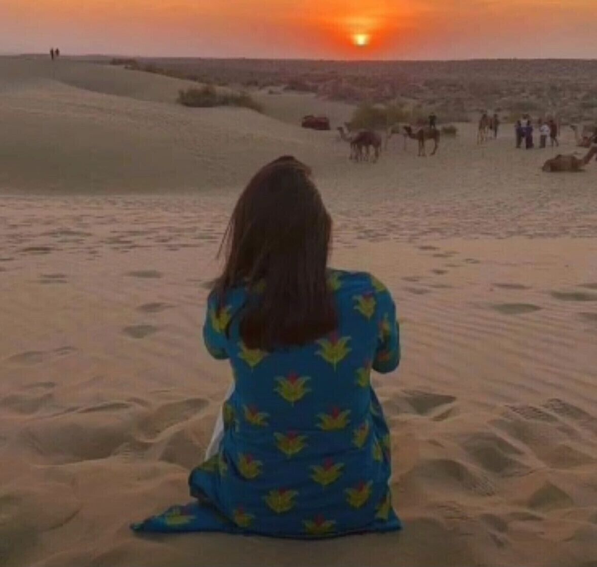 A person sitting on a sandy beach at sunset.