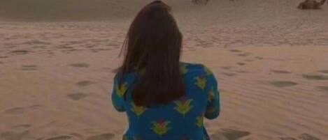 Una persona sentada en una playa arenosa al atardecer.