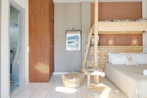 A bedroom with a bunk bed, a wooden headboard, a framed picture on the wall, and a view of a town through a window.