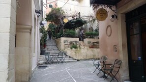 Uma rua estreita com mesas ao ar livre, uma escadaria e um prédio com placa de café.
