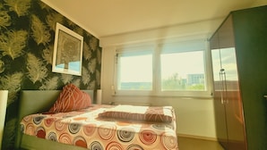 A bedroom with a bed, a window, and a green wall with a floral pattern. - Cozy 3-room vacation apartment at Dresden main station  (Dresden)