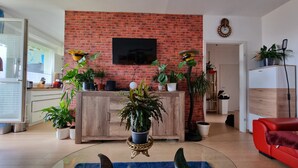 A living room with a brick wall, a flat-screen TV, wooden furniture, and various potted plants. - Cozy 3-room vacation apartment at Dresden main station  (Dresden)