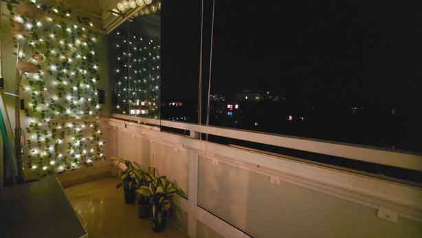 A balcony with a view of the city at night, potted plants, and a decorative wall with lights. - Cozy 3-room vacation apartment at Dresden main station  (Dresden)