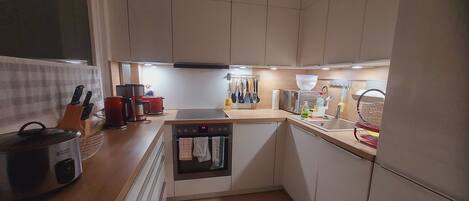 A compact kitchen with a built-in oven, a coffee maker, and a kettle on the counter.