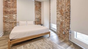 Ein modernes Schlafzimmer mit einem hölzernen Bett, Ziegelwänden und einem großen Fenster.