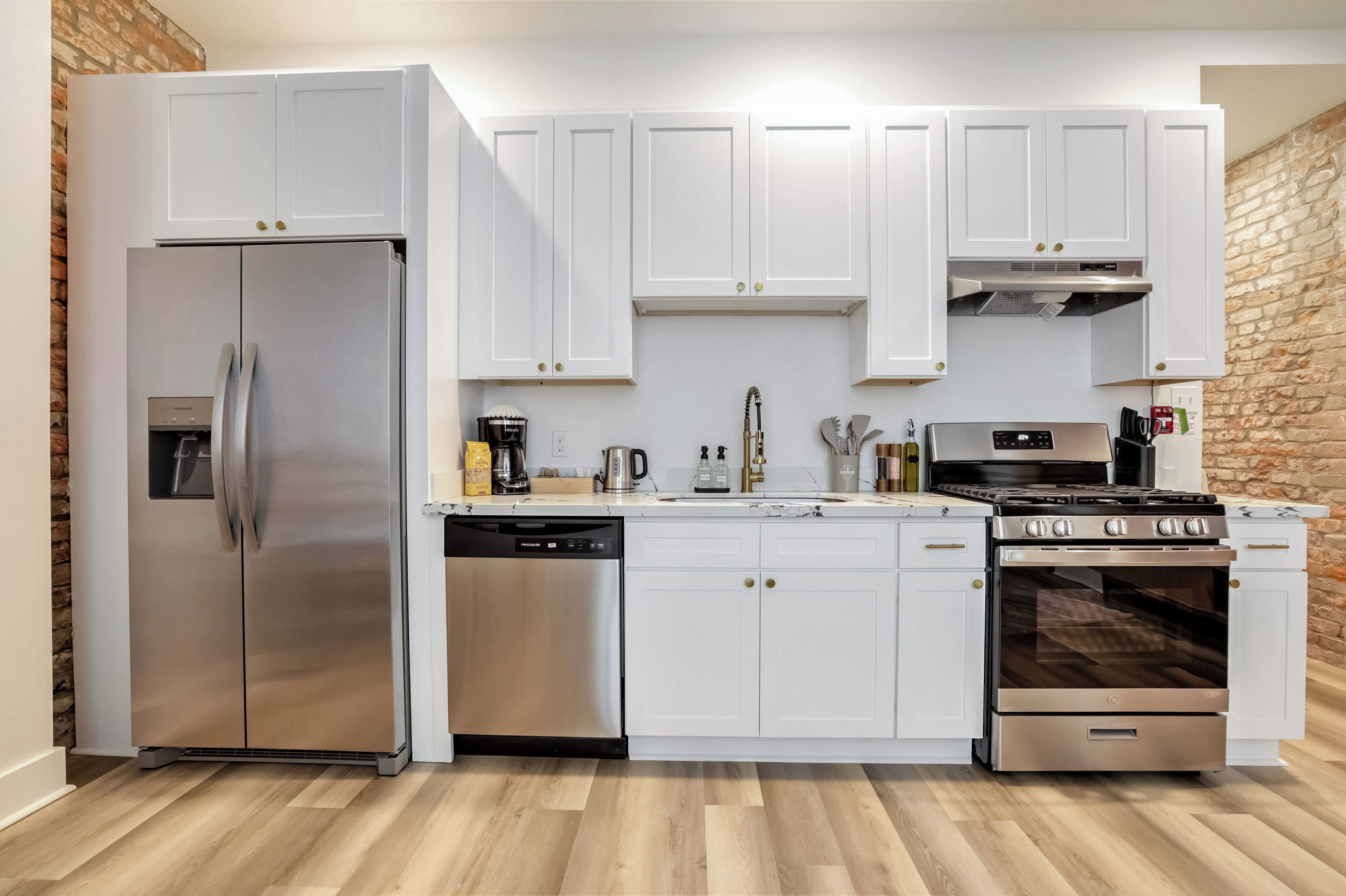 A modern kitchen with white cabinets, stainless steel appliances, and a brick wall.