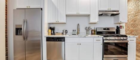 A modern kitchen with white cabinets, stainless steel appliances, and a brick wall.