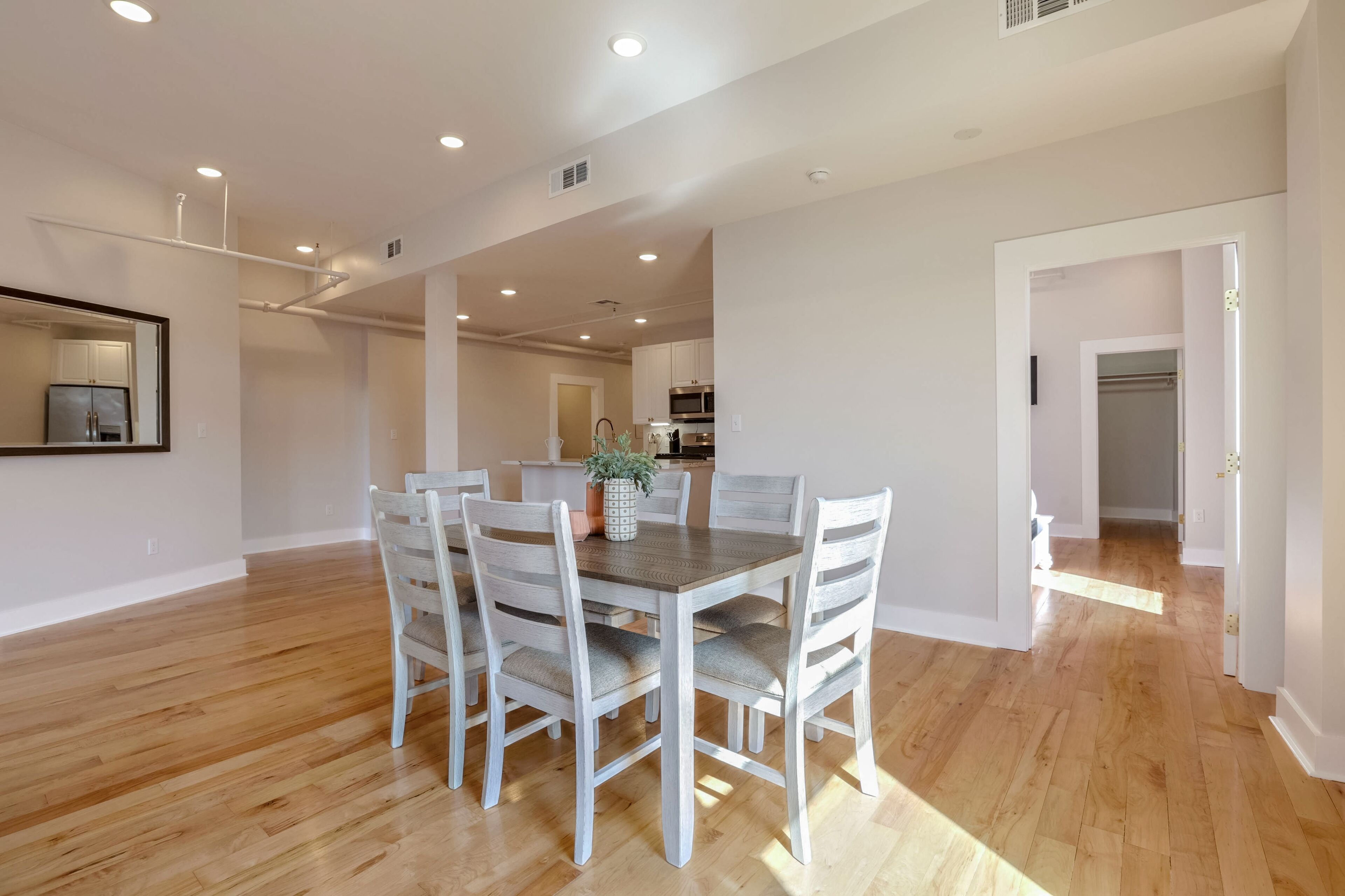 Un comedor amplio con una mesa de madera y sillas blancas, una cocina al fondo y un pasillo que conduce a otra habitación.