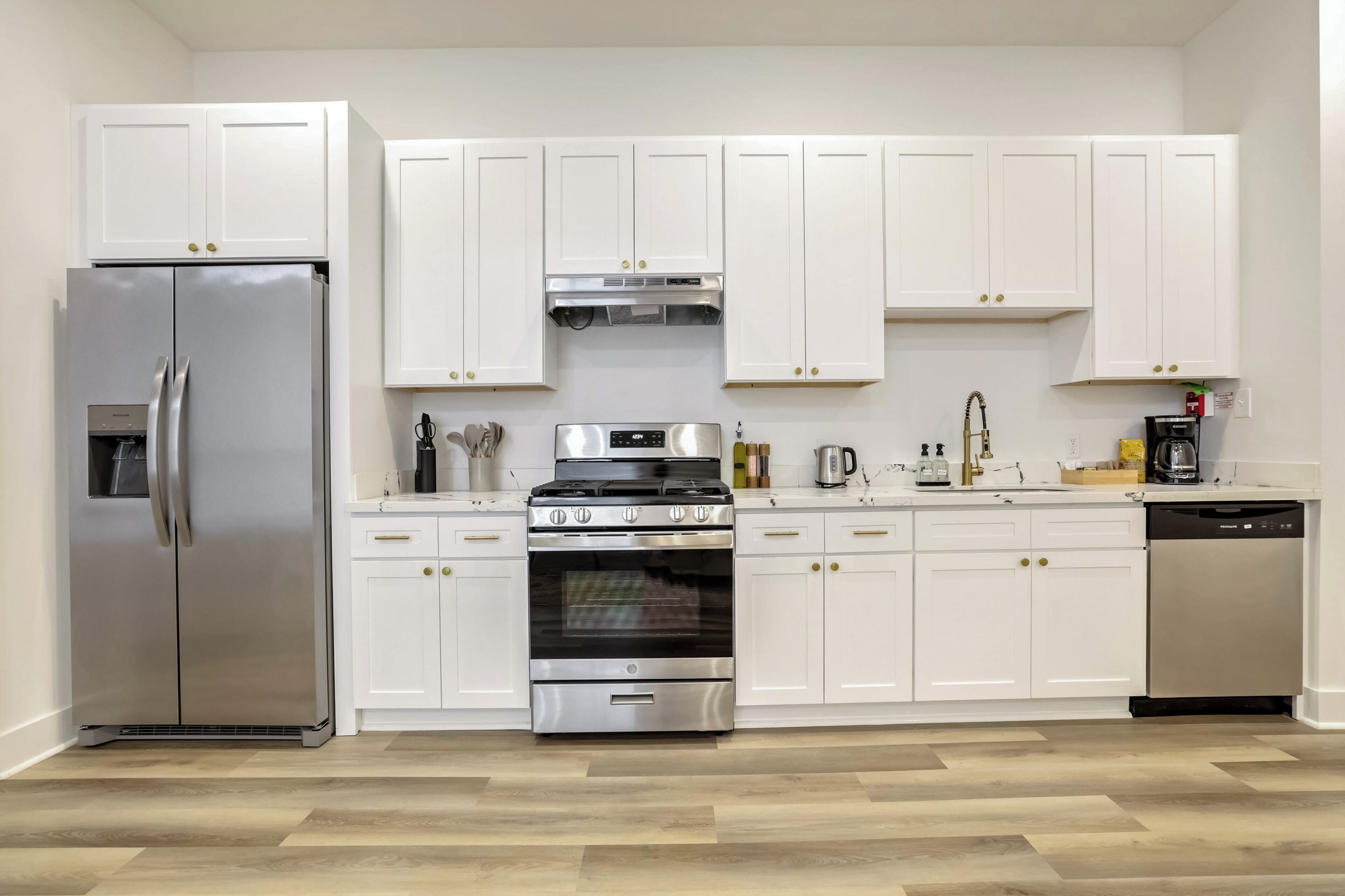 A modern kitchen with white cabinets, a stainless steel refrigerator, a gas stove, and a dishwasher.