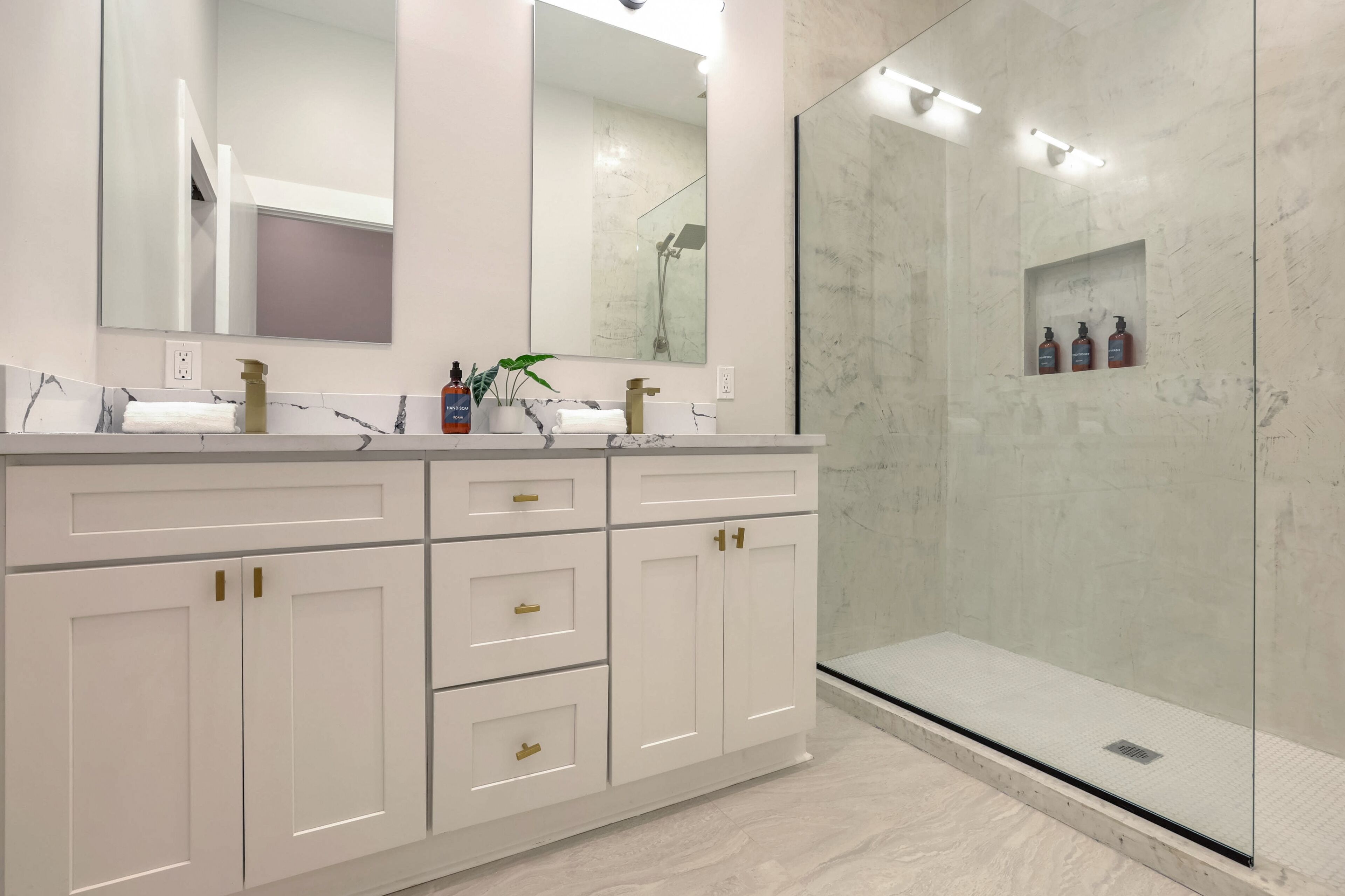 A modern bathroom with a large mirror, white cabinets, and a glass-enclosed shower.