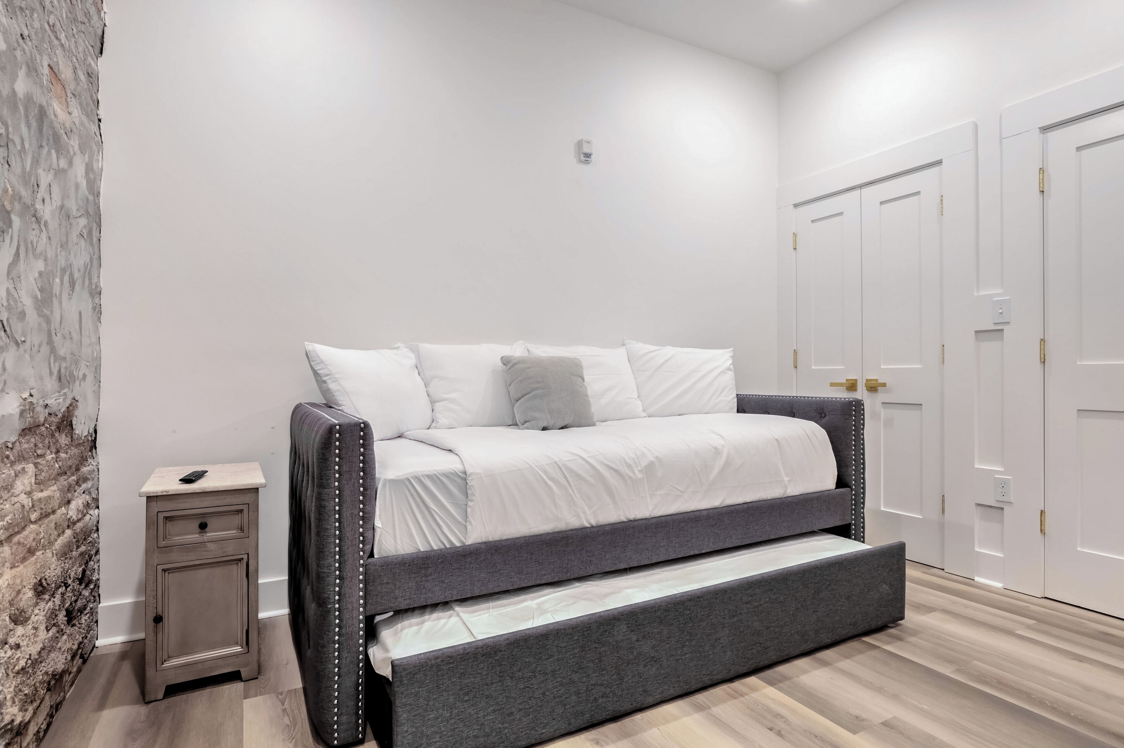 Une chambre moderne avec un canapé-lit gris, une petite table de chevet et des armoires blanches.