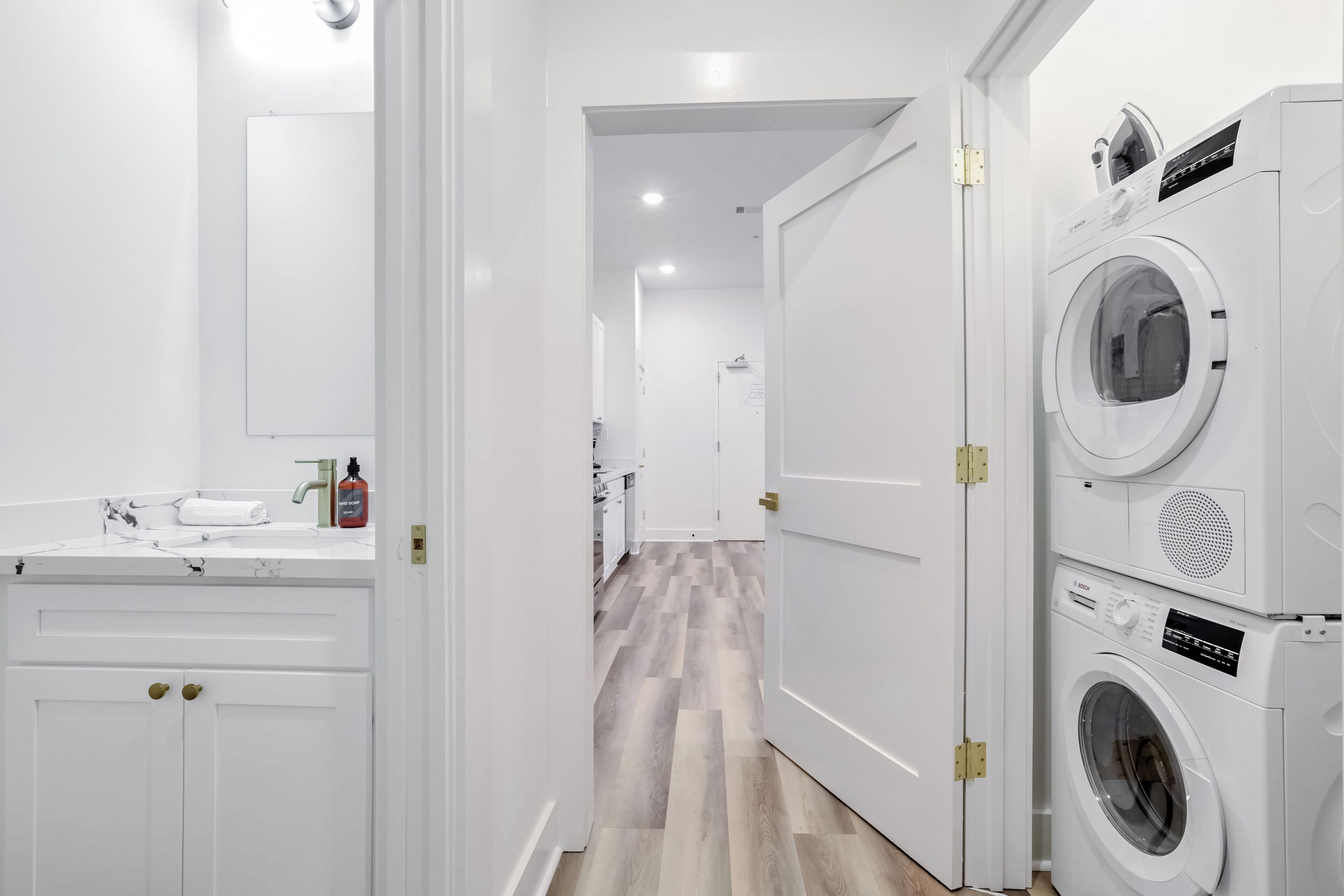 A modern laundry room with stacked washers and dryers, a white sink with a towel, and a wooden floor.