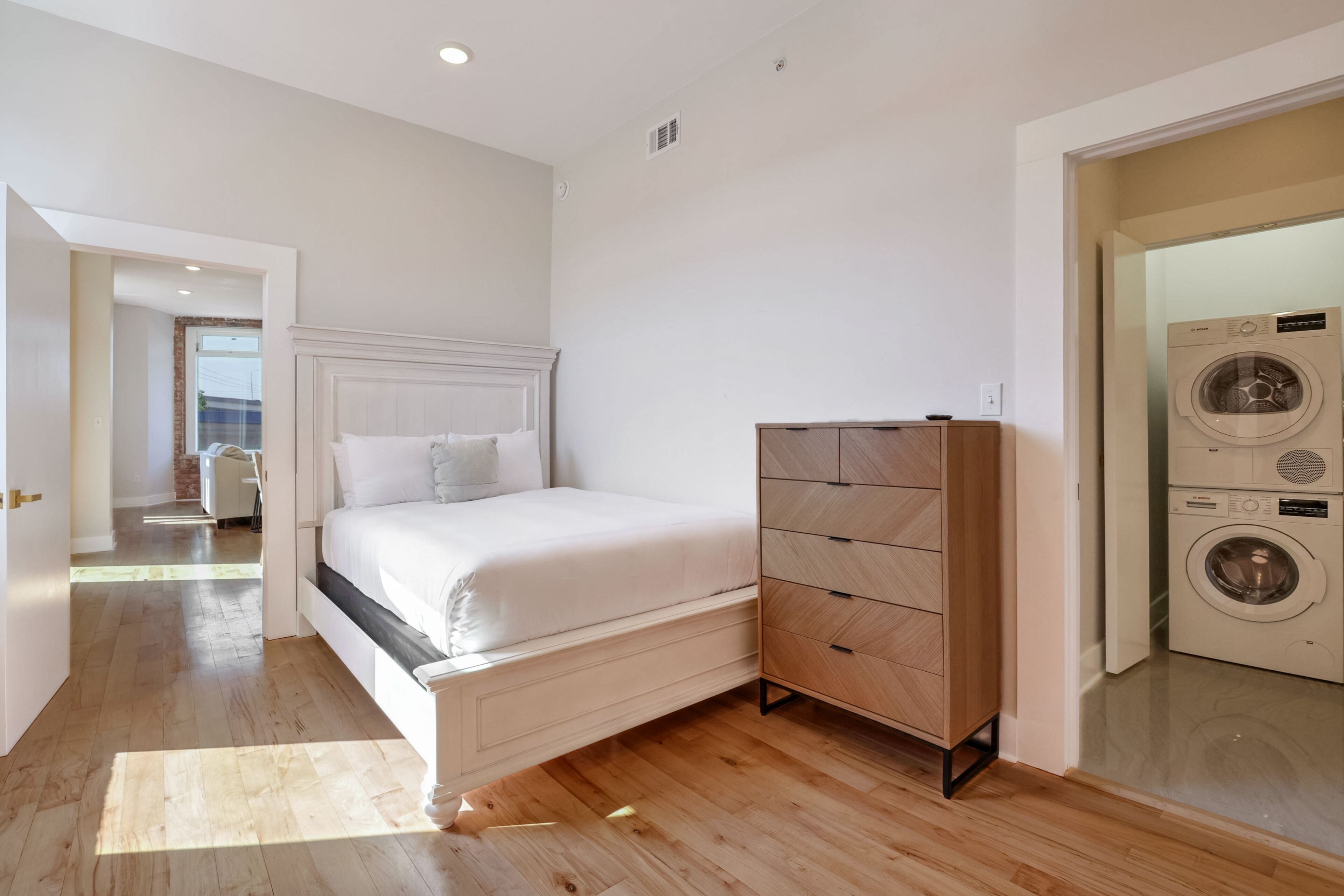 A bedroom with a bed, wooden dresser, and a washing machine.