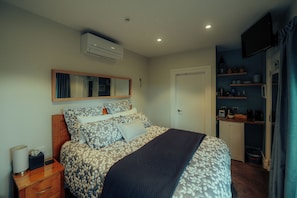 A bedroom with a bed, bedside table, mirror, wardrobe, and a small kitchenette area. - Two Rivers Boutique Lodge Ohakune (Ohakune)