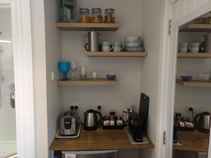 A compact kitchen with wooden shelves holding jars, cups, and a kettle. There are two toasters, a coffee maker, and a smartphone on the counter. - Two Rivers Boutique Lodge Ohakune (Ohakune)
