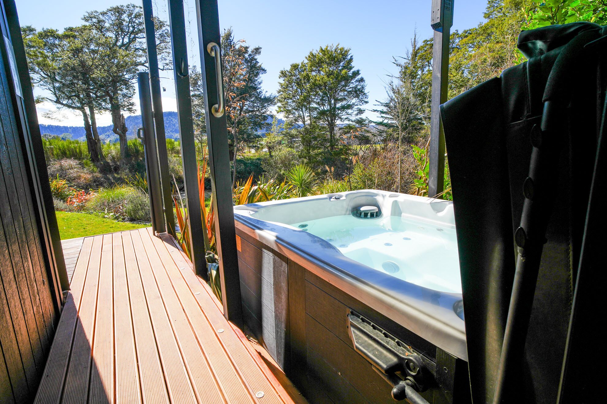 A hot tub on a wooden deck with a view of trees and mountains.