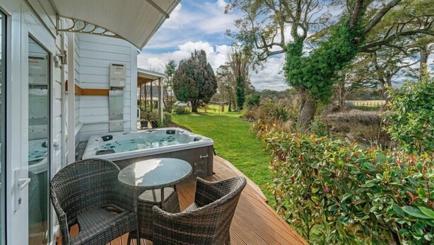 A hot tub on a wooden deck with wicker chairs, surrounded by greenery and trees. - Two Rivers Boutique Lodge Ohakune (Ohakune)