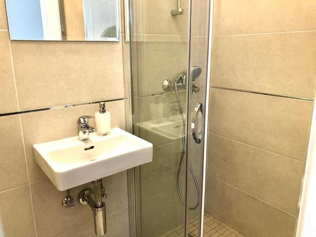 A bathroom with a glass-enclosed shower, a white sink, and a mirror above the sink.
