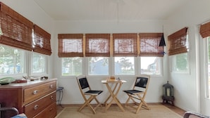 A room with a wooden dresser, two chairs, a small table, and a window with blinds. - Cove Point Beach Cottage with Chesapeake Bay Views (Lusby)