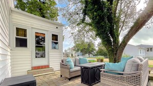 A patio area with wicker furniture and a small table, a white mobile home, and a tree in the background. - Cove Point Beach Cottage with Chesapeake Bay Views (Lusby)