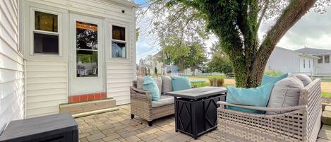 A patio area with wicker furniture and a small table, a white mobile home, and a tree in the background.