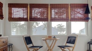 A room with three windows, a wooden table with chairs, a dresser, and a lamp. - Cove Point Beach Cottage with Chesapeake Bay Views (Lusby)
