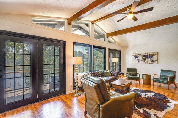 A spacious living room with a leather sofa, green chairs, a wooden coffee table, and a large rug. There are multiple windows providing natural light and views of the outdoors. - Lake O' the Pines Retreat: Private Dock! (Jefferson)