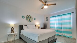 A bedroom with a bed, two bedside tables with lamps, a ceiling fan, and a striped curtain.