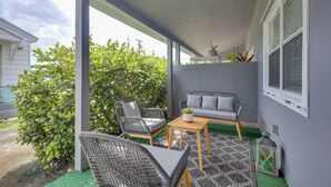 A covered patio with wicker furniture, a gray sofa, and a small table with a plant.