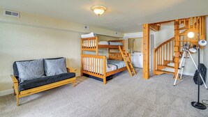 Quarto com beliches, um sofá, escada e uma mesa com luminária.