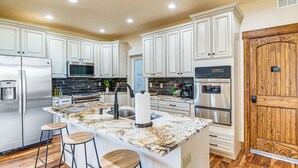 A modern kitchen with white cabinets, stainless steel appliances, a marble island, and wooden stools. - Mtn-View Home w/ Public Land Access in Guffey! (Guffey)