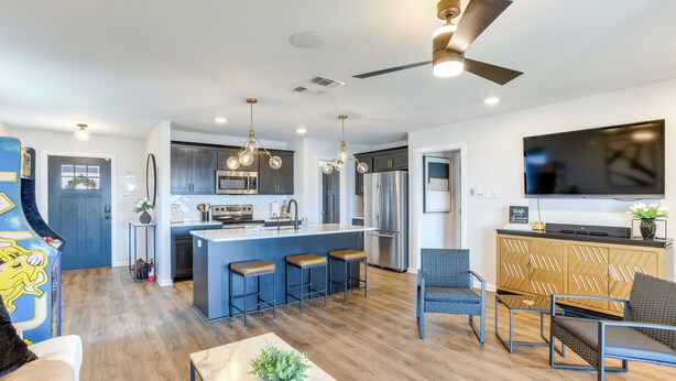 A modern kitchen with a central island, bar stools, a dining area with a table and chairs, and a living room with a sofa and a TV. - Lakefront Home w/ Dock & Patio in San Angelo! (San Angelo)