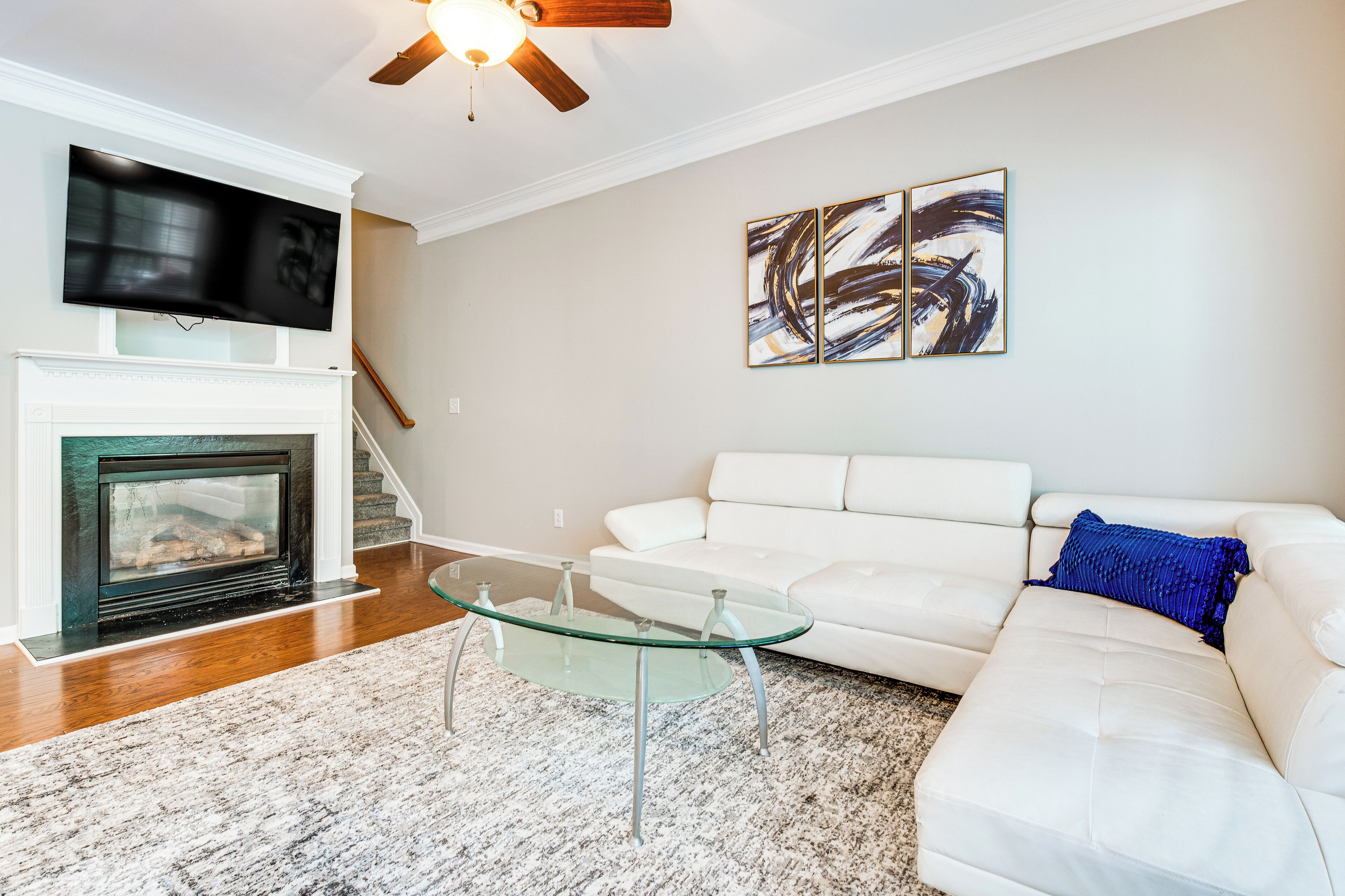 Sala de estar con chimenea, sofá blanco, mesa de centro de vidrio y arte abstracto en la pared.