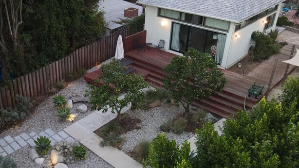 Een modern huis met een terras, omgeven door een houten hek en diverse planten.